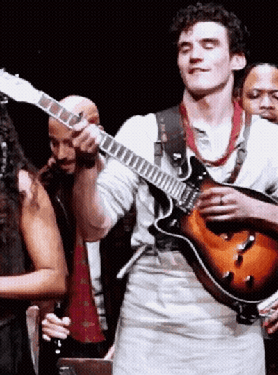 A Man Is Playing A Guitar On Stage In Front Of A Group Of People GIF