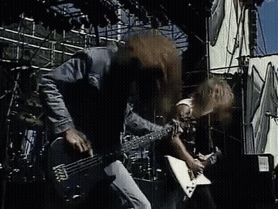 A Man Is Playing A Guitar On Stage While Another Man Drums . GIF