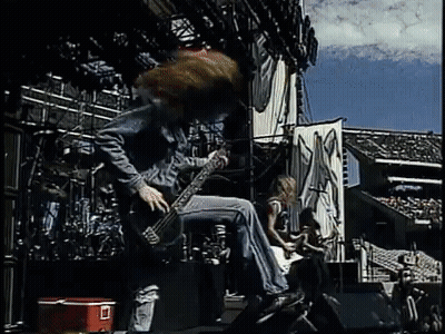 A Man Is Playing A Guitar On Stage While Another Man Plays A Guitar . GIF