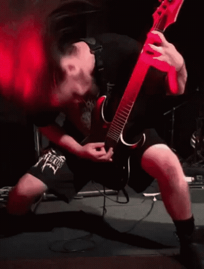 A Man Is Playing A Guitar On Stage With Red Smoke Coming Out Of His Mouth . GIF
