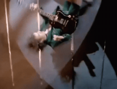 A Man Is Playing A Guitar Upside Down On A Skateboard . GIF