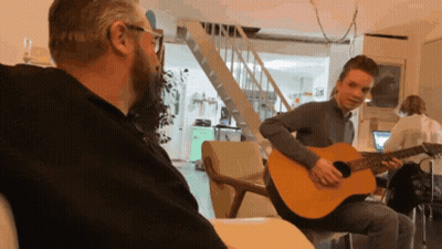 A Man Is Playing A Guitar While Another Man Looks On GIF