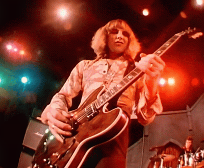 A Man Is Playing A Guitar With The Letter G On The Neck GIF