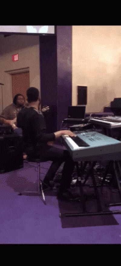 A Man Is Playing A Keyboard In A Room With An Exit Sign On The Wall GIF