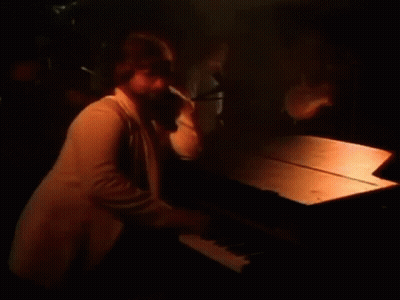 A Man Is Playing A Piano In A Dark Room With A Microphone In The Background . GIF