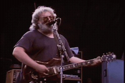A Man Is Playing A Piano On A Stage While A Band Plays Behind Him . GIF