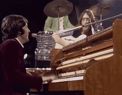 A Man Is Playing A Piano On Stage While A Drummer Plays Drums Behind Him . GIF