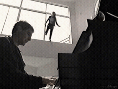 A Man Is Playing A Piano While A Woman Is Standing On A Window Sill GIF
