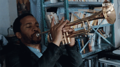 A Man Is Playing A Trumpet In Front Of A Shelf With Netflix Written On The Bottom GIF