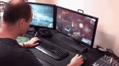 A Man Is Playing A Video Game On Two Monitors . GIF
