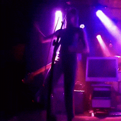 A Man Is Playing A Violin In A Dark Room With Purple Lights GIF