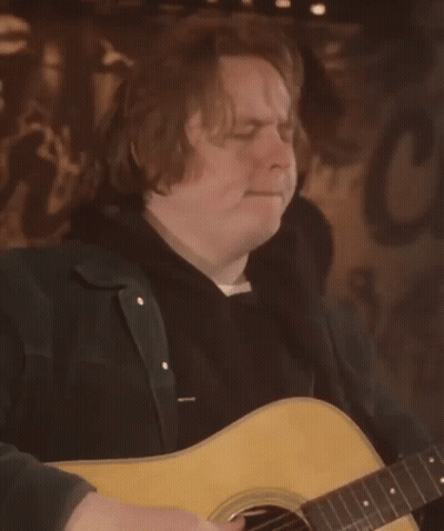 A Man Is Playing An Acoustic Guitar In Front Of A Sign That Says C GIF