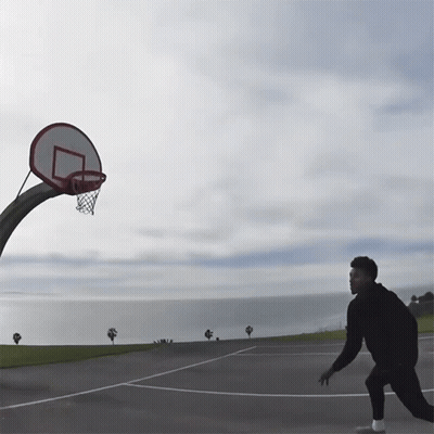 A Man Is Playing Basketball In Front Of A Basketball Hoop With The Ocean In The Background GIF