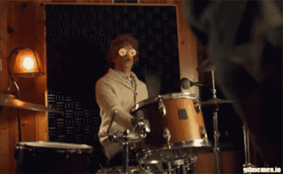 A Man Is Playing Drums In Front Of A Wall That Says Gifmemes.io On It GIF