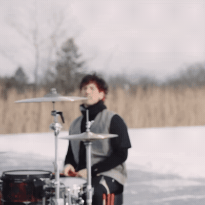 A Man Is Playing Drums In The Snow In A Field GIF
