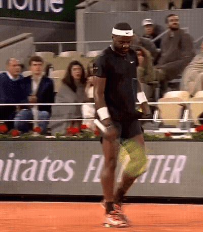 A Man Is Playing Tennis In Front Of A Banner That Says Emirates Fly Better GIF