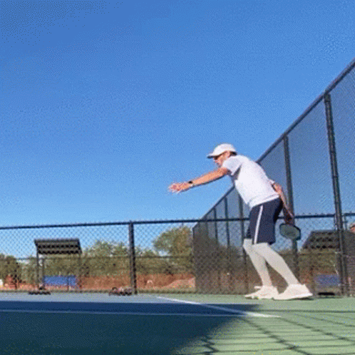 A Man Is Playing Tennis On A Court With A Blue Sky In The Background GIF