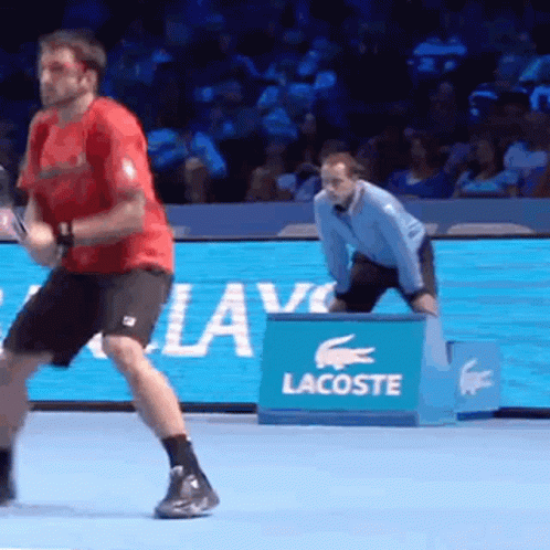 A Man Is Playing Tennis On A Court With A Lacoste Sign In The Background GIF