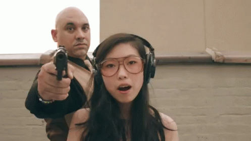 A Man Is Pointing A Gun At A Girl Wearing Headphones GIF