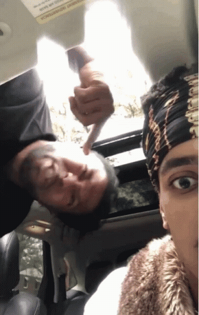 A Man Is Pointing At Another Man 'S Face In A Car With A Warning Sign On The Visor GIF