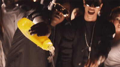 A Man Is Pouring Orange Juice Into Another Man 'S Mouth GIF