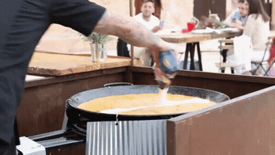 A Man Is Pouring Sauce Into A Pan With A Can Of Salsa GIF