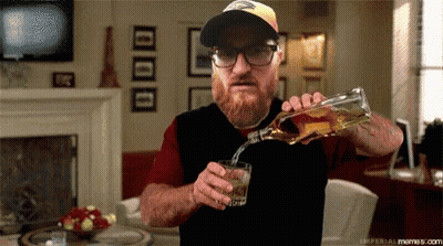 A Man Is Pouring Whiskey Into A Glass In A Living Room GIF