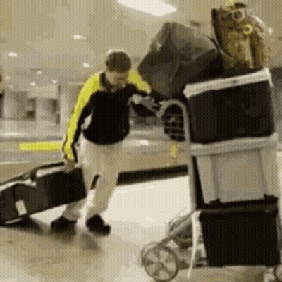 A Man Is Pushing A Cart Filled With Luggage And Boxes . GIF