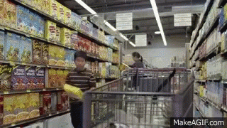 A Man Is Pushing A Shopping Cart In A Grocery Store Aisle With Boxes Of Popcorn On The Shelves GIF