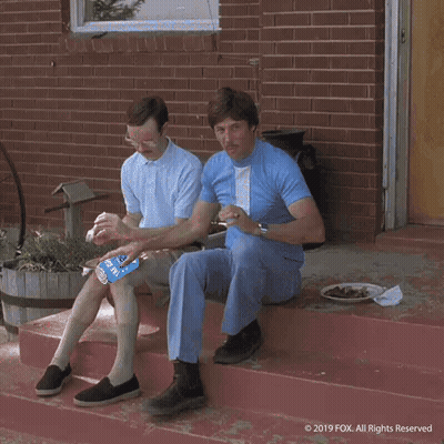 A Man Is Pushing Another Man On A Bicycle With A Bottle Of Soda On The Handlebars GIF