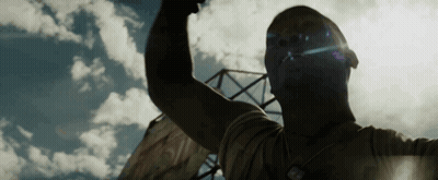 A Man Is Raising His Fist In The Air In Front Of A Blue Sky With Clouds . GIF