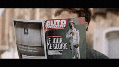 A Man Is Reading A Magazine That Says Le Jour De Gloire On The Front GIF