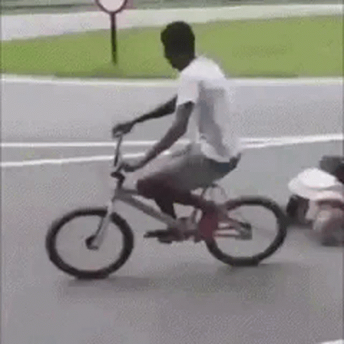 A Man Is Riding A Bicycle Down A Street Next To A Child . GIF