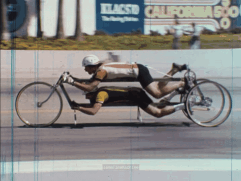 A Man Is Riding A Bicycle In Front Of A California 500 Sign GIF