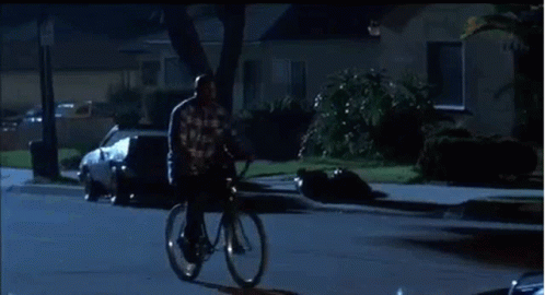 A Man Is Riding A Bike Down A City Street At Night . GIF
