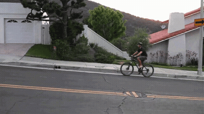 A Man Is Riding A Bike Down A Street With A Sign That Says ' No Parking ' On It GIF