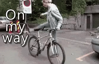 A Man Is Riding A Bike In A Parking Lot With The Words On My Way Behind Him GIF