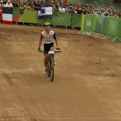 A Man Is Riding A Bike On A Dirt Track With A Crowd Behind Him GIF