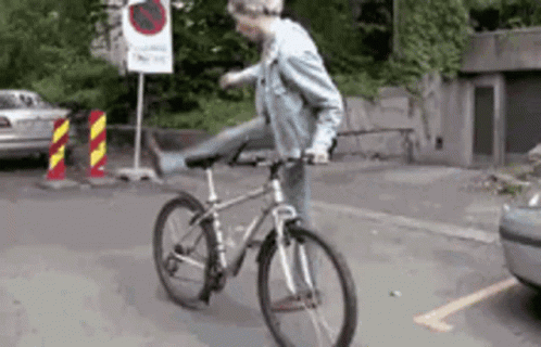 A Man Is Riding A Bike On A Street With A No Parking Sign Behind Him GIF