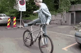 A Man Is Riding A Bike On A Street With A No Parking Sign In The Background GIF