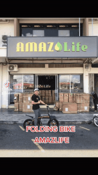 A Man Is Riding A Folding Bike In Front Of A Building That Says Amazlife GIF