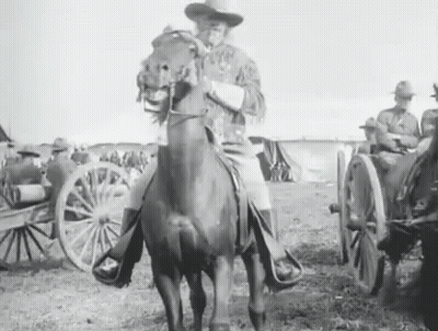 A Man Is Riding A Horse In A Field With A Wagon In The Background . GIF