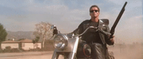 A Man Is Riding A Motorcycle Down A Dirt Road While Holding A Helmet . GIF
