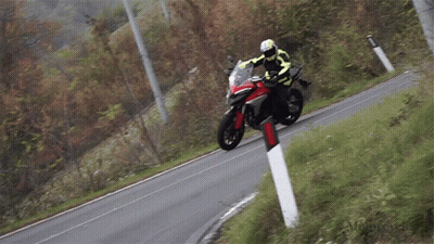 A Man Is Riding A Motorcycle Down A Road With A Red And Black Stripe On The Side GIF