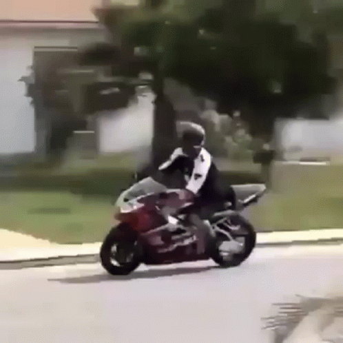 A Man Is Riding A Motorcycle Down A Street In Front Of A House . GIF
