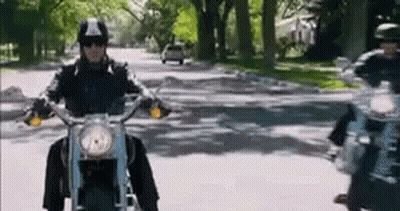 A Man Is Riding A Motorcycle Down A Street With Trees In The Background . GIF