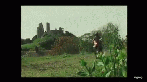 A Man Is Riding A Motorcycle In A Field In Front Of A Castle . GIF