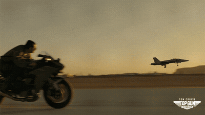 A Man Is Riding A Motorcycle In Front Of An Airplane That Says Top Gun Maverick GIF