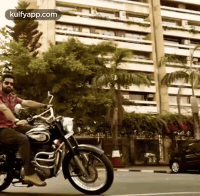 A Man Is Riding A Motorcycle On A City Street . GIF