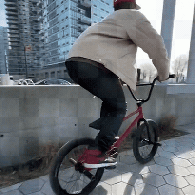 A Man Is Riding A Red Bike On A Sidewalk GIF